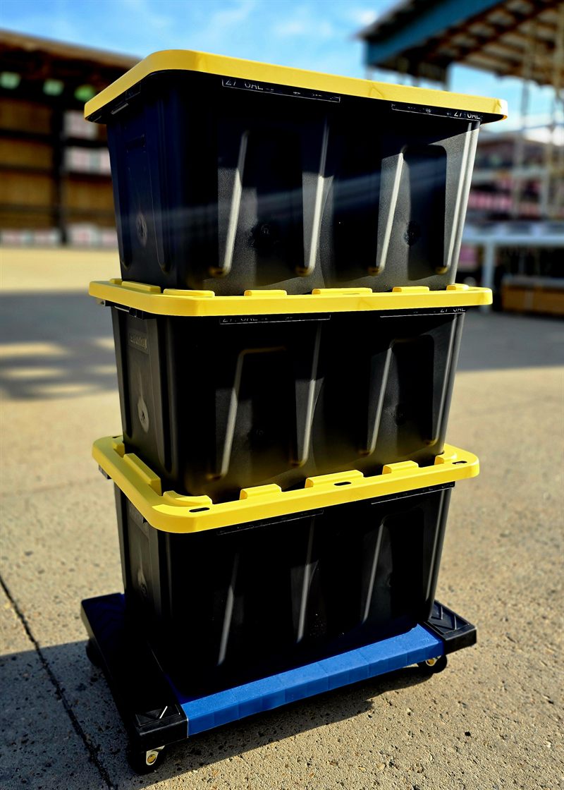 Three black moving totes with yellow lids stacked on a blue Tote Cart